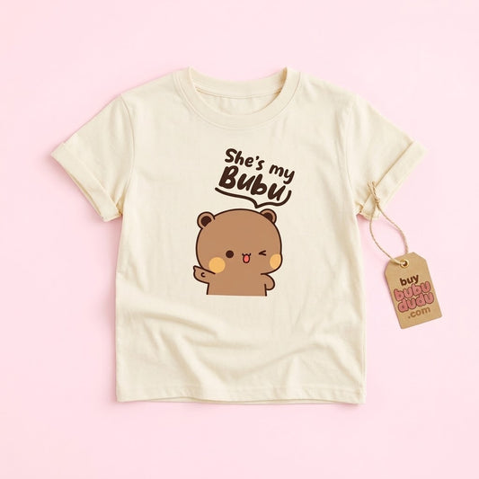 A cream-colored short-sleeve t-shirt with a cute cartoon bear graphic and the text 'She's my Bubu'. The shirt is displayed flat on a light pink background with a brown paper hangtag attached to the sleeve.