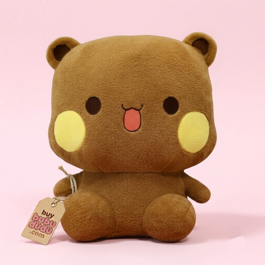 A brown plush bear toy with yellow circular cheeks, a pink tongue, and black eyes, sitting against a solid pink background. A paper tag reading 'buy BUBBEGO.