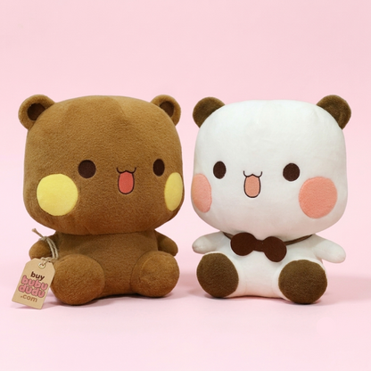 Two cute plush toys side by side on a solid pink background. On the left is a brown bear plush with yellow cheeks and a pink tongue, featuring a hanging tag that reads 'buy big bitches plush'.