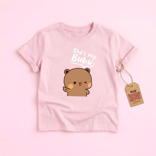 A light pink short-sleeve t-shirt with a cute cartoon bear graphic and the text 'She's my Bubu'. A brown paper hangtag is attached to the right side of the shirt.